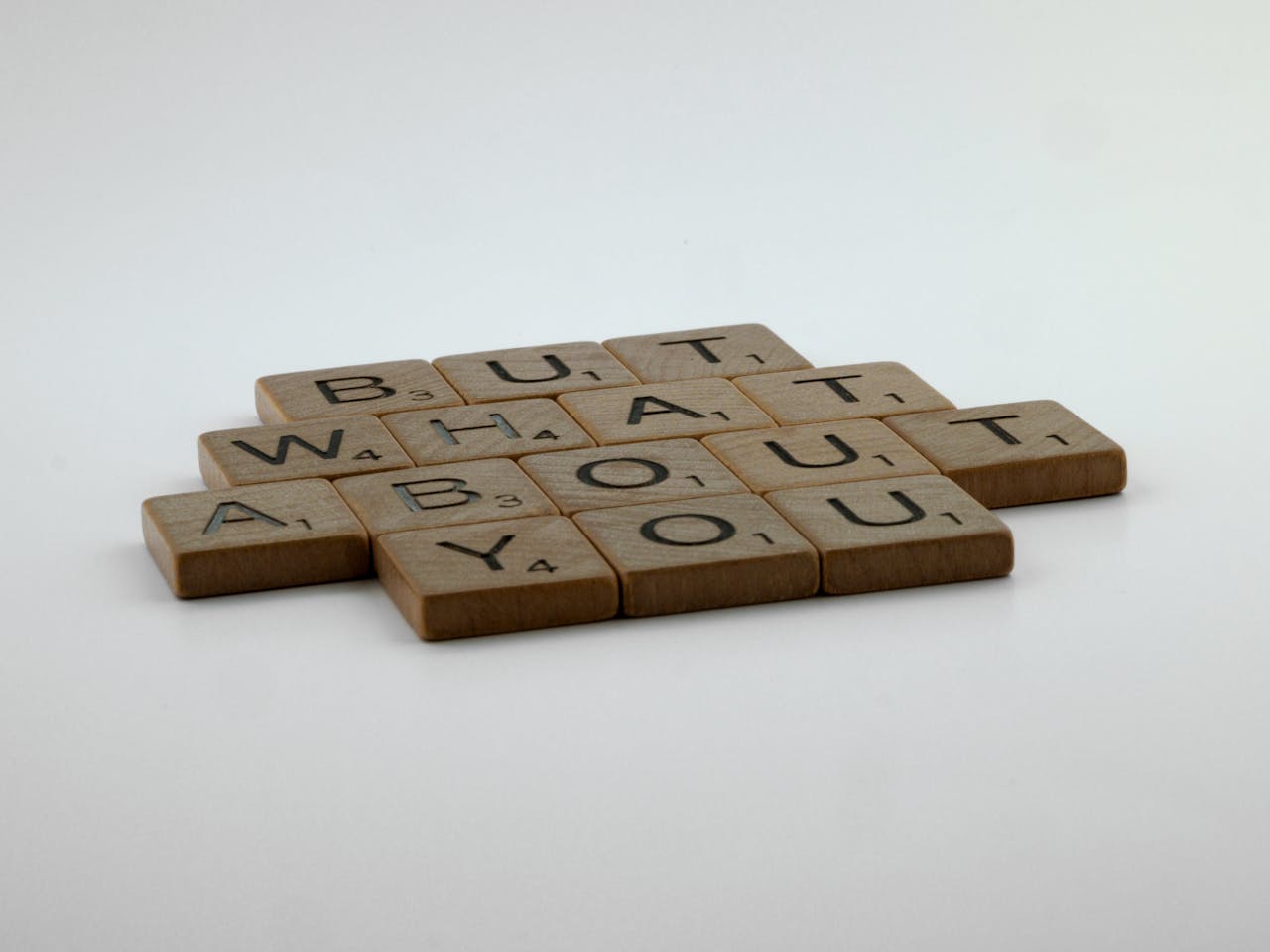 Wooden Scrabble tiles spelling out 'But What About You' on a white background.