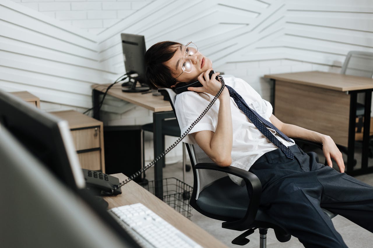 Asian call center agent relaxing on chair while talking on phone in an office setting. Business environment.